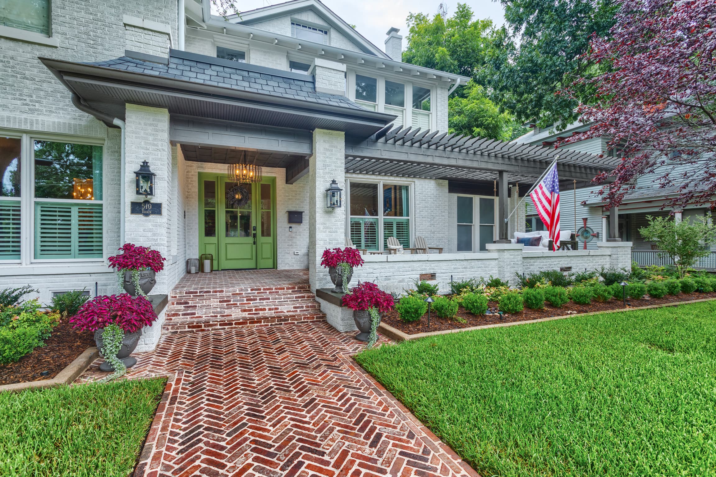 White brick house with a green door, herringbone brick walkway, and an American flag.