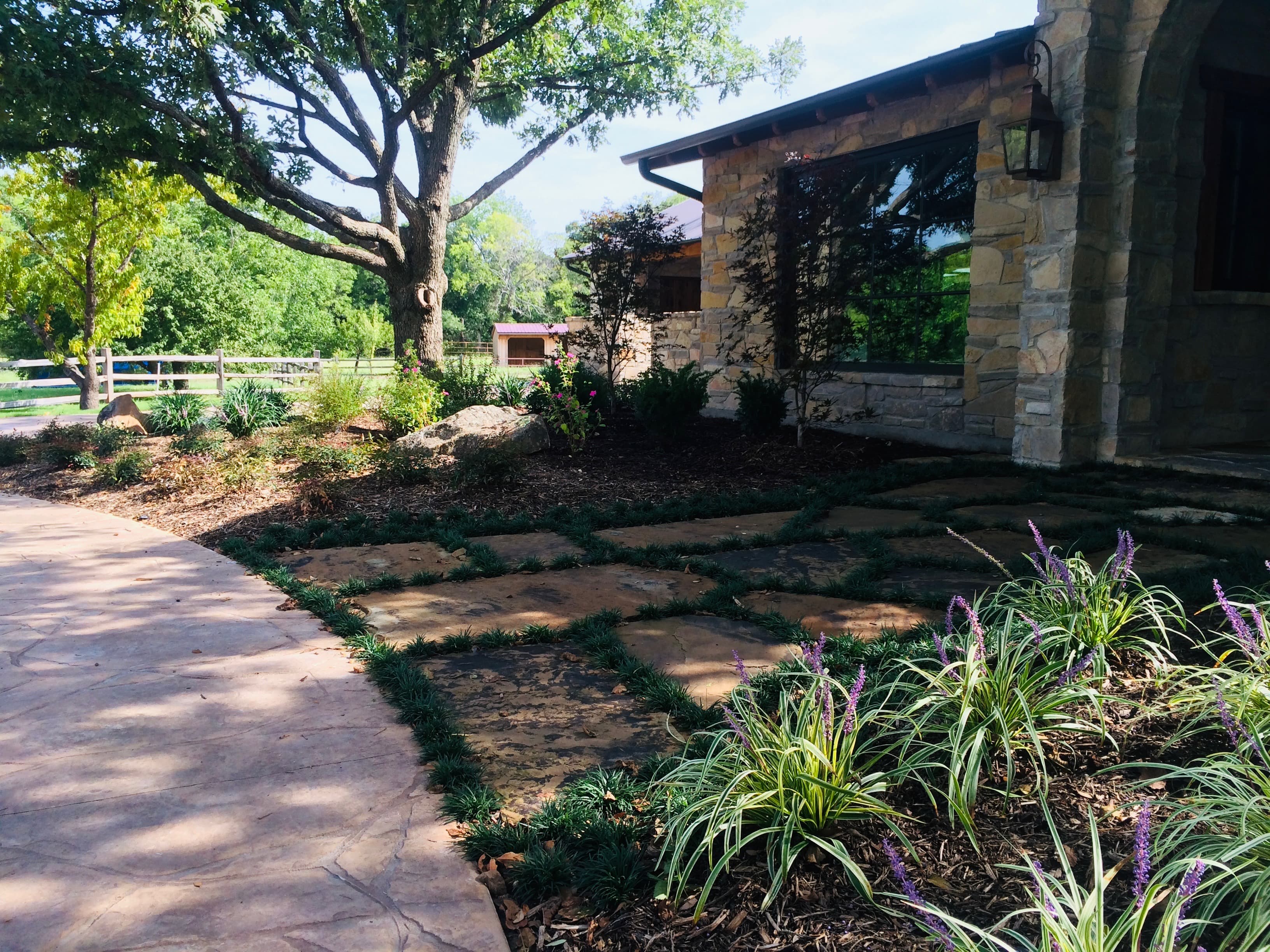 Stone house with large window overlooking landscaped garden with flagstone paths and purple flowers.