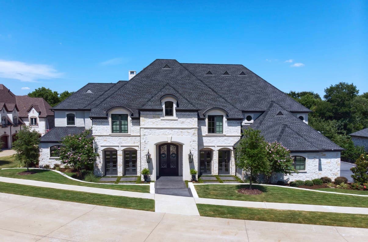 Luxurious white stone mansion with a dark gabled roof, arched windows, and green lawn.