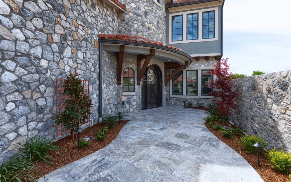 Stone house entrance with an arched door, curved tile awning, and a gray stone walkway.