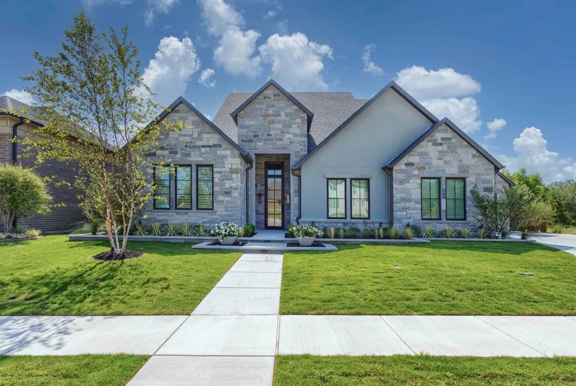 Modern grey stone house with multiple gables, black-framed windows, and a lush green front lawn.
