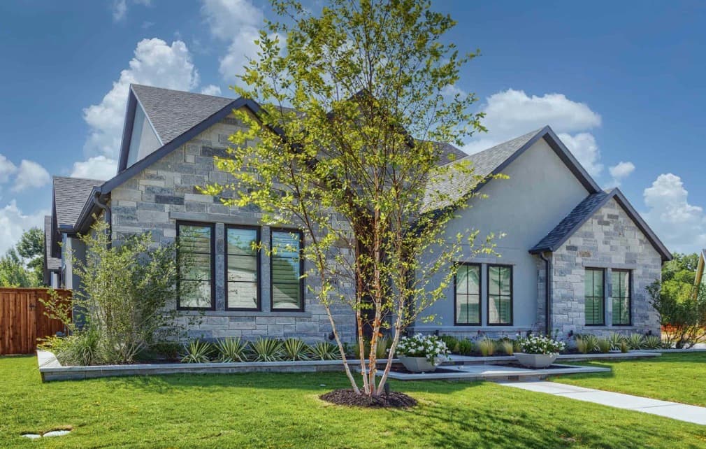 Modern grey stone and stucco home with dark windows and a manicured front lawn.