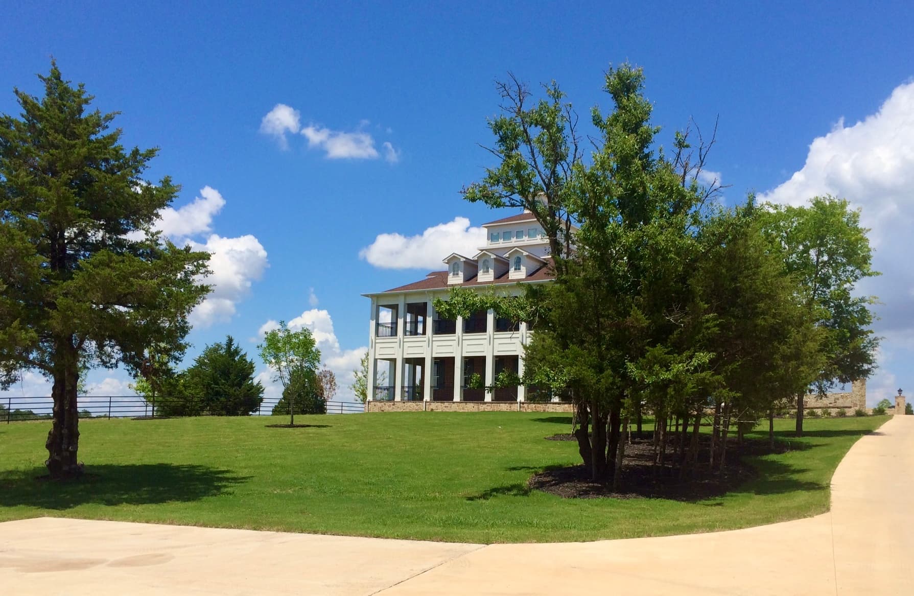 Large white multi-story building on a green lawn under a blue sky with white clouds.