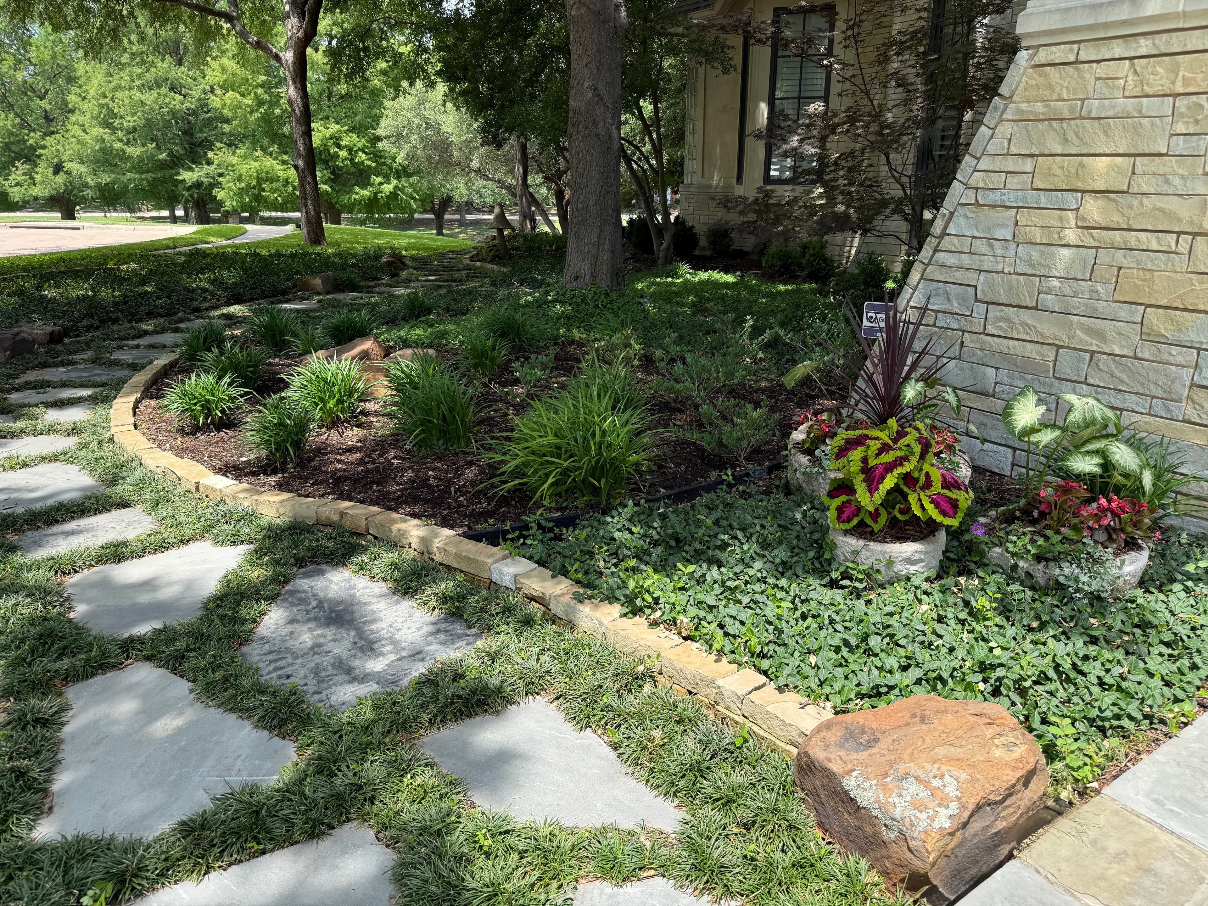 Flagstone path curves through a lush garden with colorful plants and a stone wall.