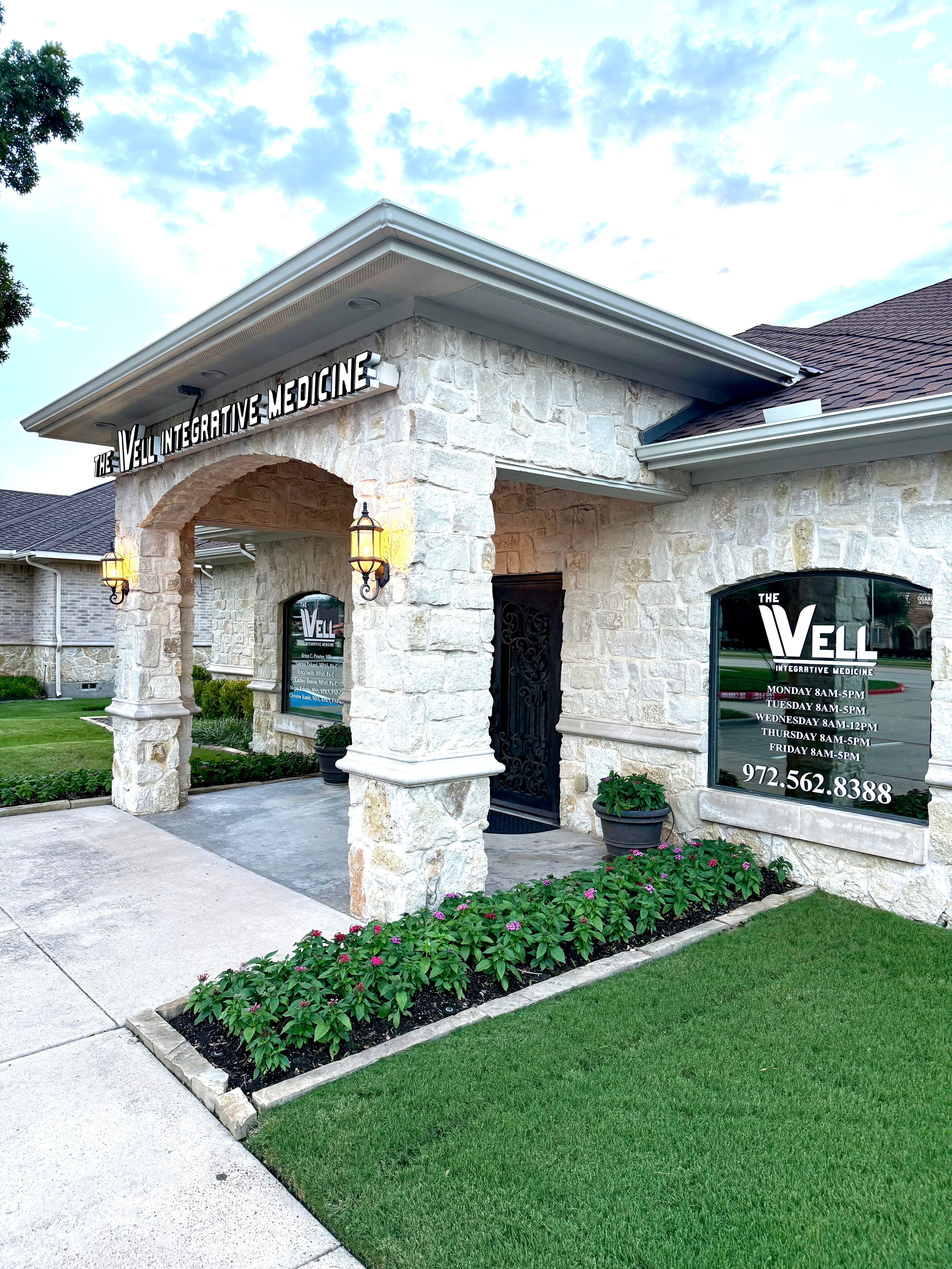 The Well Integrative Medicine stone building with arched entryway, lanterns, and pink flower landscaping.