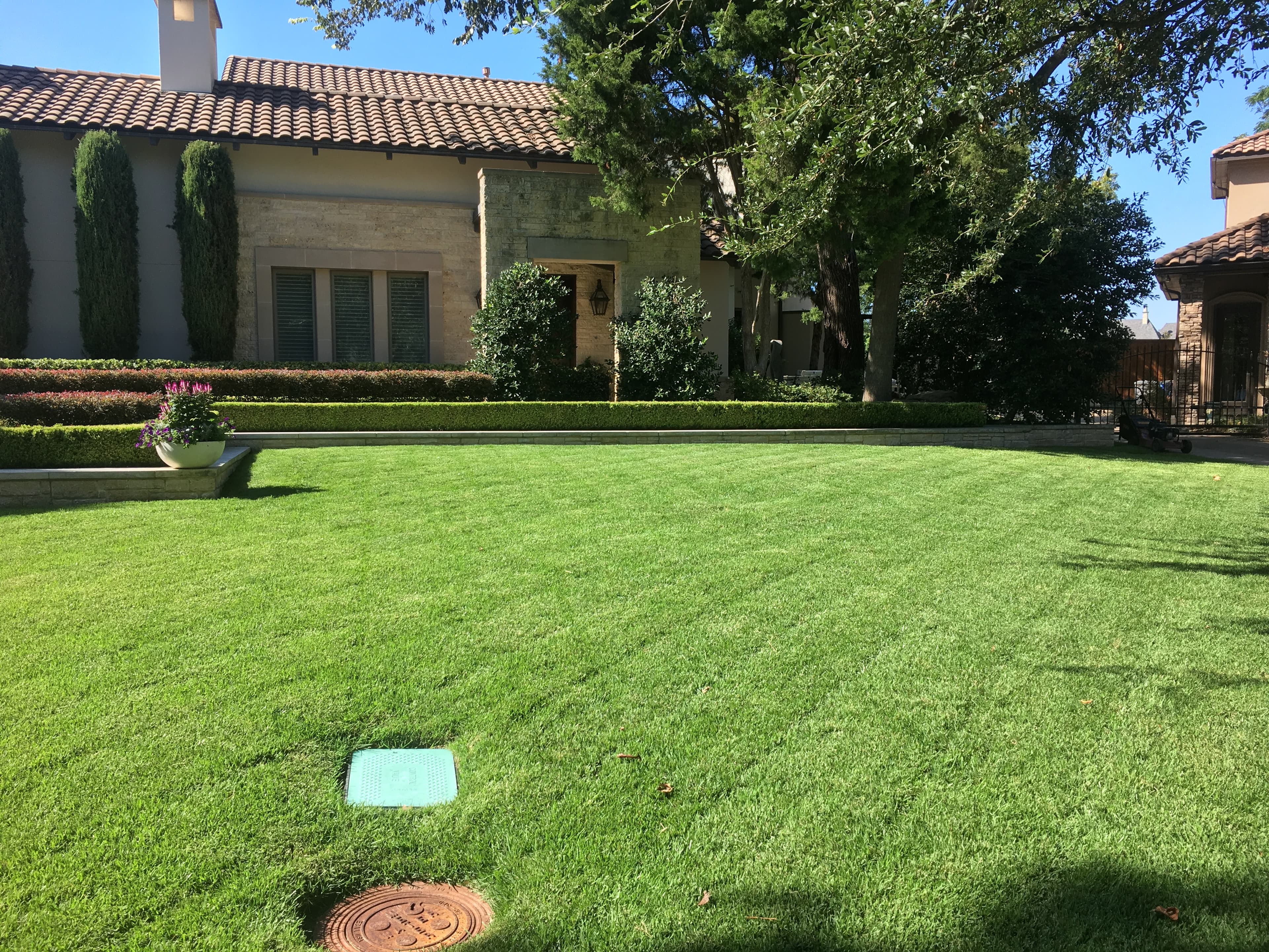 Manicured green lawn in front of a Mediterranean-style house with a terracotta tile roof.