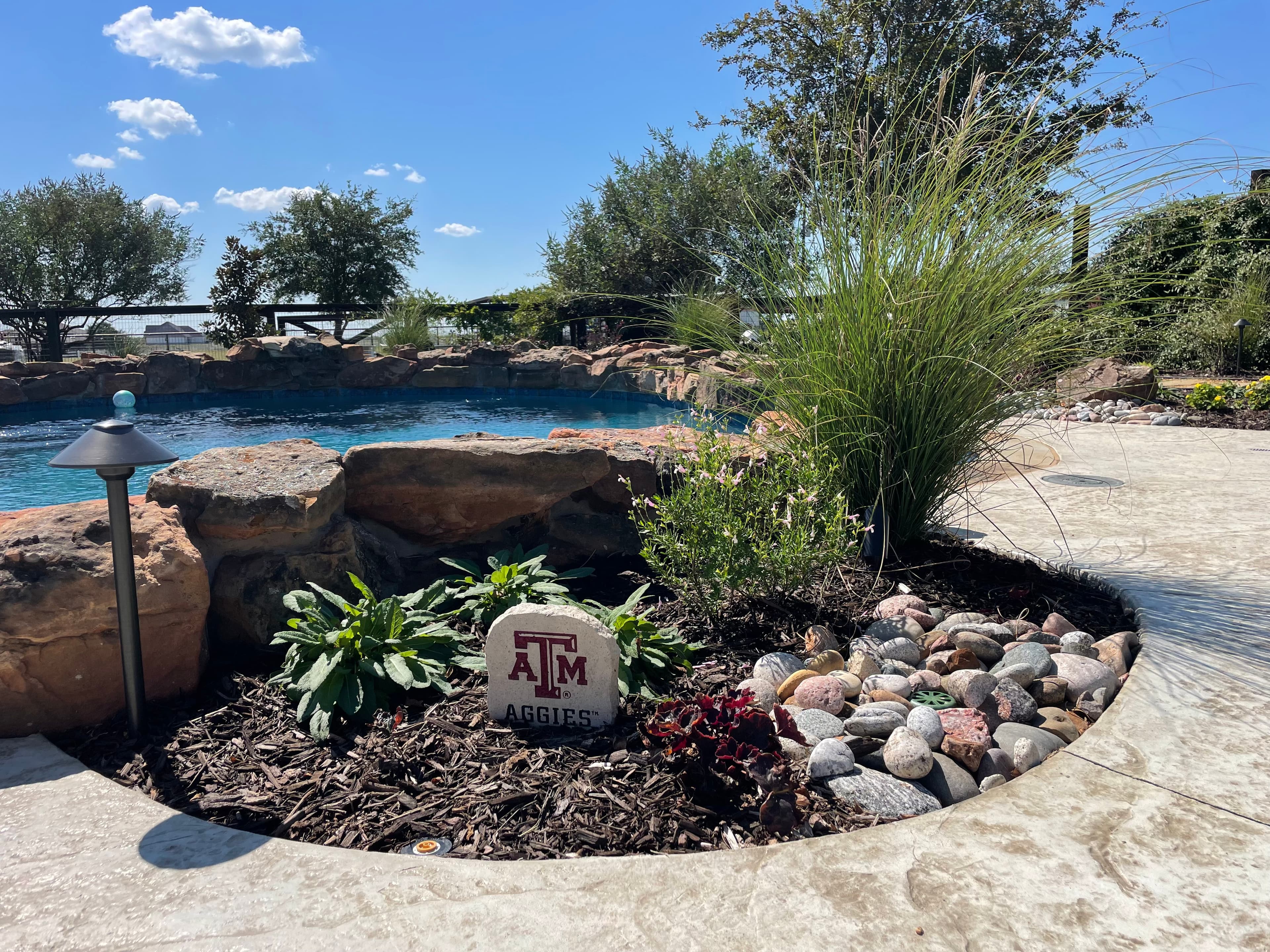 Texas A&M Aggies stone in a landscaped garden bed next to a swimming pool.