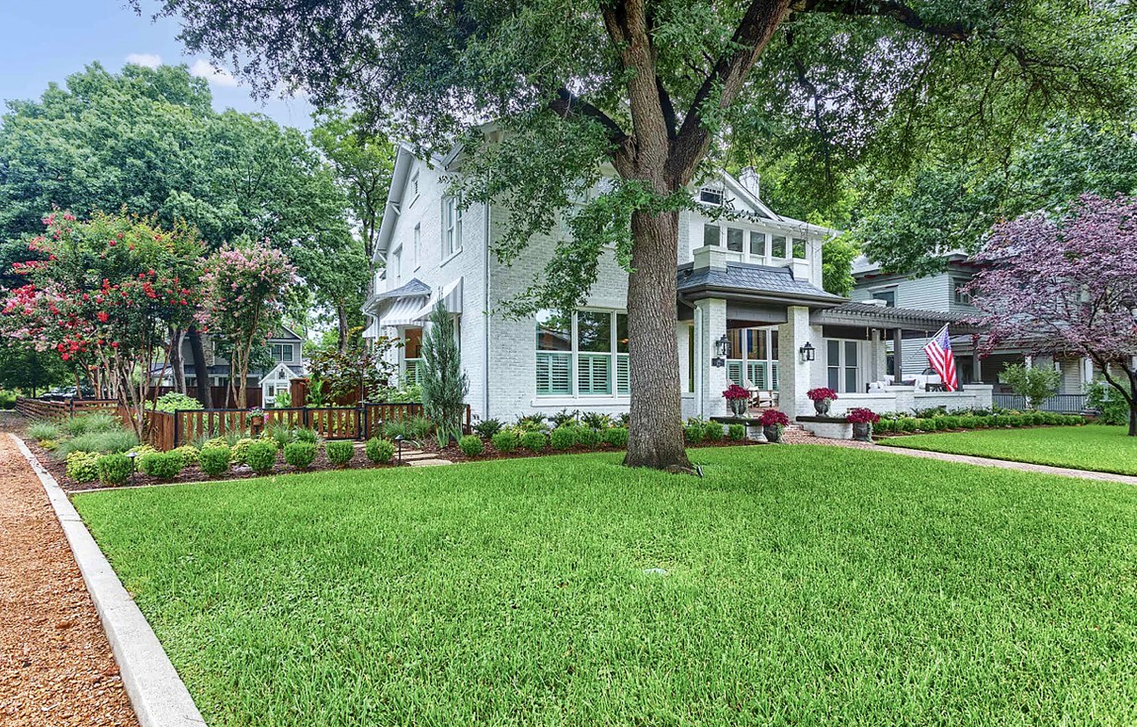 Stately white brick home featuring a lush green lawn, mature trees, and an American flag.